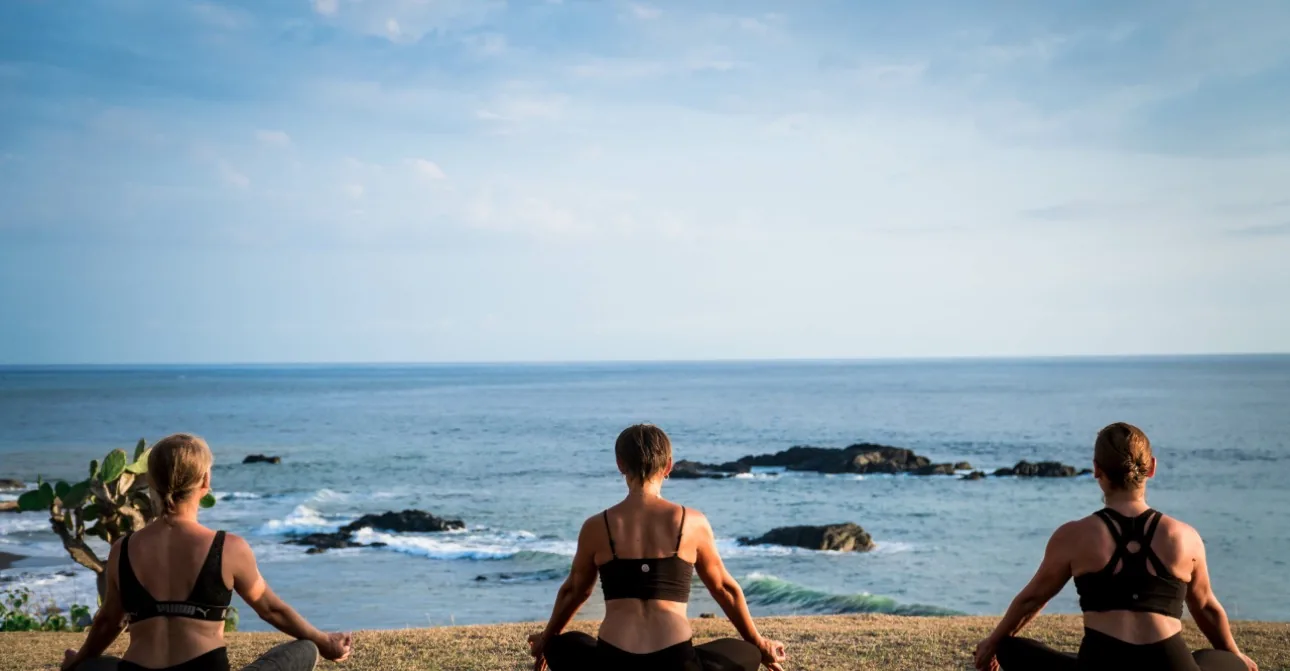 Three people seated in meditation on the grass, facing the Pacific